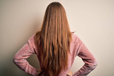 Genç, güzel, kızıl saçlı, pembe bir süveter giyen, izole edilmiş beyaz bir arka planı olan, kolları vücudunda geriye doğru bakan bir kadın.