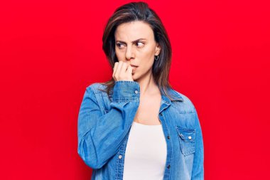 Gündelik kıyafetler giyen genç ve güzel bir kadın gergin görünüyor ve elleri ağızdan tırnak yiyor. anksiyete. 