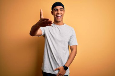 Yakışıklı Afro-Amerikan sporcusu sarı arka plan üzerine spor giysisi giyerek selamlama ve hoş geldin demek için gülümseyerek tokalaşıyor. Başarılı bir iş..