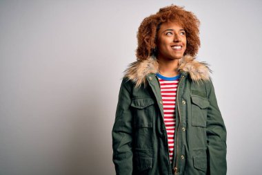 Kıvırcık saçlı, yeşil montlu genç, güzel Afro-Amerikan kadın yüzünde gülümseme, doğal bir ifade ile yan yana bakıyor. Kendinden emin gülen.