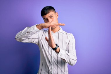 Zarif iş gömleği giyen genç yakışıklı İspanyol adam mor arka planda duruyor. Elleriyle, hayal kırıklığına uğramış ve ciddi bir yüz ifadesiyle jest yapıyor.