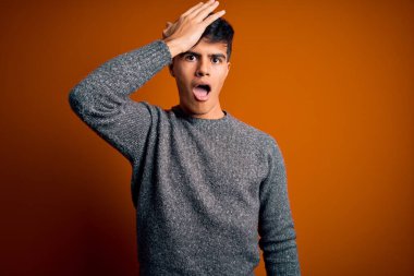 İzole edilmiş turuncu arka planda dikilen sıradan süveter giyen genç yakışıklı bir adam hata sonucu el ele tutuşarak şaşırdı. Hatayı hatırla. Unuttum, kötü hafıza konsepti.