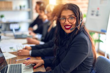 Group of call center workers working together with smile on face using headset. Young beautiful woman smiling at the office.