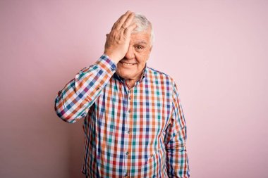 Kıdemli yakışıklı, beyaz gömlekli, soyutlanmış pembe arka planda, bir gözünü kapayan, yüzünde kendine güvenen bir gülümseme ve sürpriz bir duygu var..