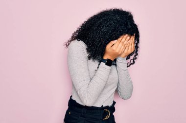 Genç Afro-Amerikan kadın balıkçı yaka kazak ve pembe arka planda gözlük takıyor ve ağlarken suratını ellerle kapatıyor. Depresyon kavramı.