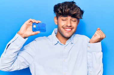 Genç İspanyol adam kredi kartı tutuyor gururla bağırıyor, zaferi kutluyor ve başarıyı kollarını kaldırarak kutluyor. 