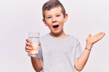 Sevimli sarışın çocuk bir bardak su içerek başarıyı kutluyor mutlu bir gülümsemeyle ve kazanan el kaldırarak ifade ediyor. 
