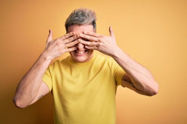 Sarı arka plan üzerine sarı tişört giyen genç, yakışıklı ve modern bir adam. Gözleri neşeli ve komik gülümseyerek kapatıyor. Kör kavram.