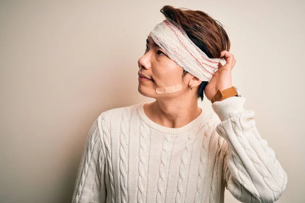 Young handsome chinese man injured for accident wearing bandage and strips on head confuse and wondering about question. Uncertain with doubt, thinking with hand on head. Pensive concept.