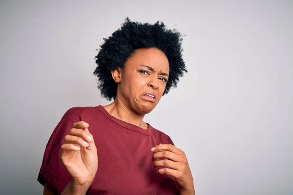 Young beautiful African American afro woman with curly hair wearing casual t-shirt standing disgusted expression, displeased and fearful doing disgust face because aversion reaction. With hands raised