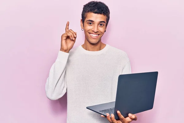 若いアフリカ系アメリカ人の男がノートパソコンを持っている幸せな顔をしたアイデアや質問を指差す指で驚いて ナンバーワン — ストック写真