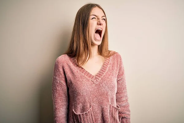 若い美しい赤毛の女性がピンクのカジュアルなセーターを着て孤立した白い背景に怒りと怒りを叫び 怒りで叫んで怒っている 激怒と積極的な概念 — ストック写真