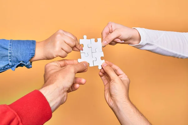 Hands of caucasian young people connecting pieces of puzzle over isolated yellow background