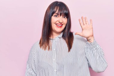 Genç ve cüsseli kadın gündelik kıyafetler giyer ve beş numarayı göstererek gülümserken kendinden emin ve mutlu görünürdü.. 