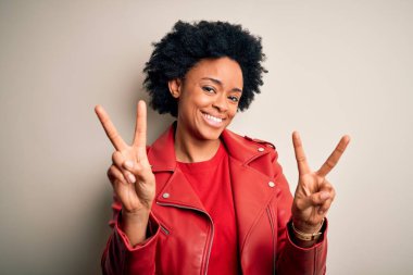Kıvırcık saçlı, sıradan kırmızı ceketli, kameraya bakıp zafer işareti yapan güzel Afro-Amerikan kadın. İki numara..