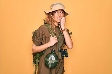 Sırt çantası ve su matarası takan mavi gözlü genç sarışın kaşif elleri ağızda tırnak yerken gergin ve stresli görünüyor. Endişe sorunu.