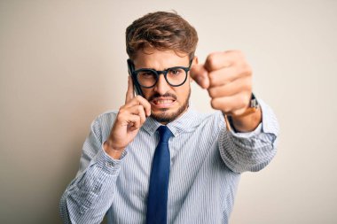 Genç işadamı beyaz arka plan üzerinden akıllı telefondan konuşuyor. Sinirli ve sinirli bir şekilde bağırıyor, çıldırıyor ve el kaldırarak bağırıyor. Öfke kavramı.