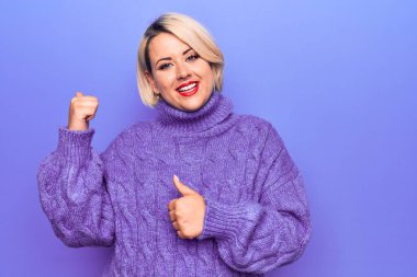 Güzel sarışın ve cüsseli bir kadın mor arka planda balıkçı yaka kazak giyiyor. Arka tarafı işaret ediyor. El ve baş parmakları havada, kendinden emin gülümsüyor.