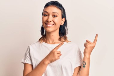 Gündelik kıyafetler giyen, gülümseyen ve kameraya bakan genç bir kadın iki eliyle ve parmaklarıyla kenarı işaret ediyor.. 