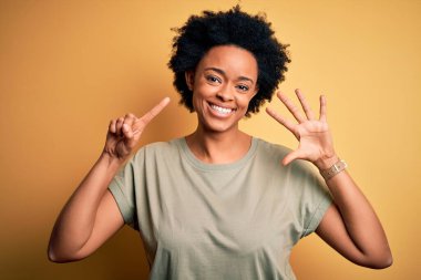 Kıvırcık saçlı, sıradan tişörtlü, genç, Afro-Amerikan bir kadın. Altıncı parmaklarını gösterirken, kendinden emin ve mutlu gülümserken..