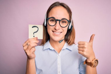 Güzel çağrı merkezi ajanı kadın, elinde kulaklıkla çalışıyor. Soru işareti var. Mutlu, gülümsüyor.