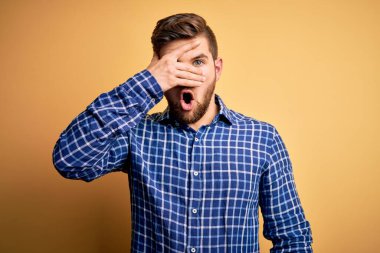 Sarışın, sakallı ve mavi gözlü genç bir işadamı sarı arka planda gömlek giyiyor. Şok olmuş bir şekilde yüzünü ve gözlerini kapıyor. Utanmış bir ifadeyle parmaklarının arasından bakıyor..