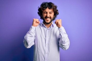 Mor arka planda dikilen sakallı yakışıklı iş adamı kolları havada ve gözleri kapalı zaferi kutlarken heyecanla bekliyor. Kazanan konsept.