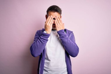 Pembe arka planda duran mor kazak ve gözlük giyen genç yakışıklı adam yorgunluk ve baş ağrısı için gözlerini ovuşturuyor, uykulu ve yorgun bir ifade takınıyor. Görüş sorunu