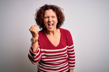 Orta yaşlı güzel kıvırcık saçlı kadın beyaz arka plan üzerine normal çizgili süveter giyiyor kızgın ve kızgın yumruğunu kaldırıyor ve öfkeyle bağırıyor. Öfke ve agresif kavram.