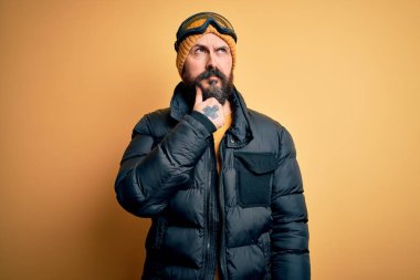 Sakallı, kar maskesi takan, kar maskesi takan ve çenesi çenesinde kayak gözlüklü yakışıklı, kel bir adam soru sormayı düşünüyor, düşünceli bir ifade. Düşünceli bir yüzle gülümsüyor. Şüphe kavramı.