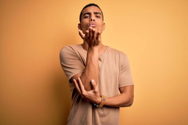 Genç, yakışıklı, Afro-Amerikalı bir adam sarı arka planda dikilmiş kameraya bakarken havada el ele öpüşmek güzel ve seksi oluyor. Aşk ifadesi.