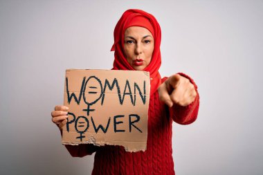 Orta yaşlı kadın, kadın hakları için tesettürlü. Elinde kameraya işaret eden bir pankart var. Ve sen, el işareti, ön taraftan olumlu ve kendinden emin bir hareket.