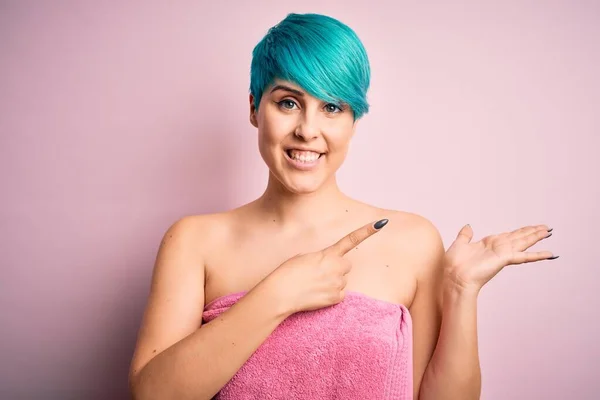 ピンクを背景にシャワーの後にタオルを身に着けて青いファッションの髪を持つ若い女性は驚きと手で提示しながら カメラに笑顔と指で指して — ストック写真