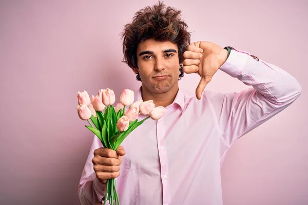 若いですハンサムな男は花が上に立っている孤立したピンクの背景で怒っている顔 否定的なサインを示し嫌いで親指ダウン 拒絶概念 — ストック写真