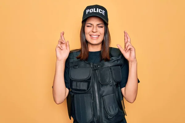 年轻美丽的黑发女警察身穿警服 身穿防弹衣 头戴帽子 摆好姿势 微笑着与希望交手 闭上眼睛 运气和迷信观念 — 图库照片