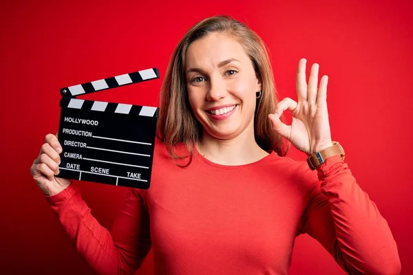 Joven Hermosa Rubia Clapper Mujer Sosteniendo Clapboard Sobre Fondo Rojo —  Fotos de Stock