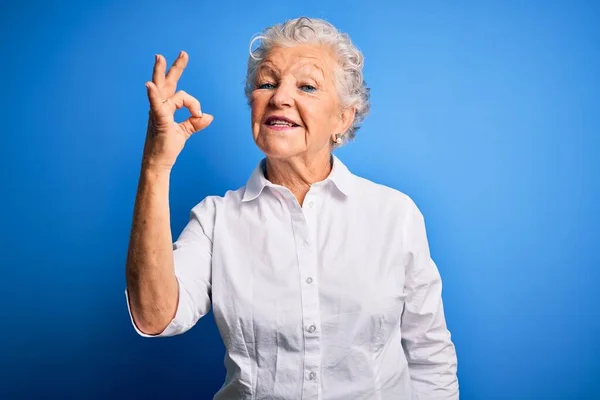 年长的漂亮女人穿着雅致的衬衫 站在孤立的蓝色背景上 微笑着 手指手画脚地做着确定的手势 成功表达 — 图库照片