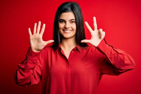 年轻美丽的黑发女子穿着休闲装 站在红色的背景上 露出八号手指 面带微笑 自信而快乐 — 图库照片