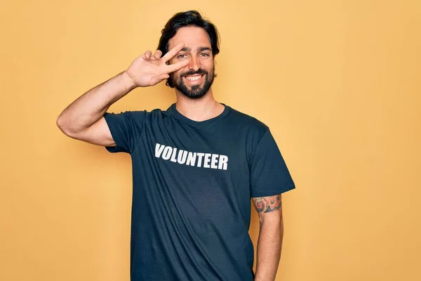 若いハンサムなパニックボランティア男性ボランティアTシャツを社会的ケアとして身に着けています顔の上に指で平和のシンボルを行います 明るい勝利を示す笑顔 — ストック写真
