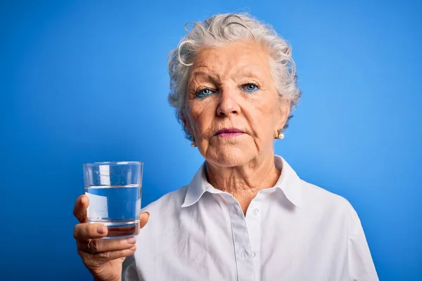 シニア美女飲むガラスの水スタンド上隔離された青の背景とともに自信を持って表現上のスマート顔思考真剣に — ストック写真