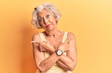 Üst düzey gri saçlı kadın her iki tarafı da parmaklarıyla göstererek farklı yönlere bakıyor. 