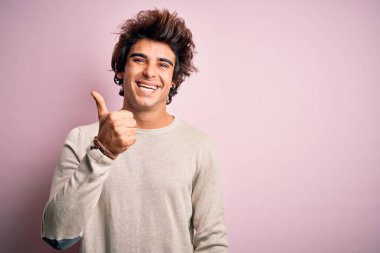 İzole edilmiş pembe arka plan üzerinde sıradan tişörtler giyen genç yakışıklı adam mutlu bir el hareketi yapıyor. Kameraya bakıp başarıyı gösteren ifade onaylanıyor.