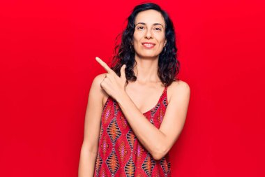 Genç ve güzel İspanyol kadın, günlük kıyafetler giyiyor. Gülümsüyor, eli ve parmağı yana doğru uzanıyor. 