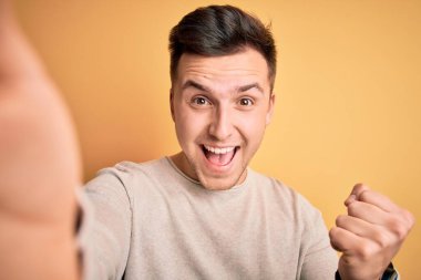 Sarı arka planda selfie çeken yakışıklı beyaz adam gururla bağırıyor ve zaferi ve başarıyı kutluyor. Çok heyecanlı, coşkulu bir duygu.