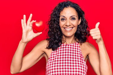 Orta yaşlı, kalbi olan güzel bir kadın mutlu ve pozitif gülümsüyor, başparmağıyla mükemmel ve onay işareti yapıyor. 
