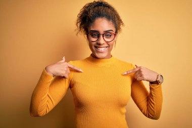 Sarı arka planda süveter ve gözlük takan genç ve güzel Afro-Amerikalı kız yüzünde bir gülümsemeyle, gururlu ve mutlu bir şekilde kendini işaret ediyor..