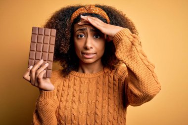 Afro saçlı, sarı arka planda çikolata tutan Afro-Amerikalı genç bir kadın. Elleri başının üstünde, utanç ve şaşkınlık dolu, sinirli ve hayal kırıklığına uğramış. Hata için korku ve üzüntü.