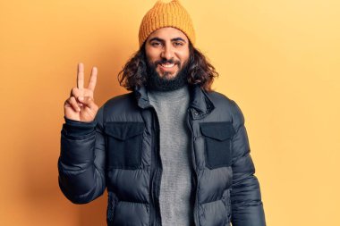 Gündelik kışlık giysiler giyen genç bir Arap kameraya gülümseyen ve zafer işareti yapan bir adam. İki numara.. 