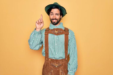 Almanya Festivali için geleneksel Alman Ekim Festivali kıyafeti giyen yakışıklı genç adam bir numarayı gösterip işaret ederken kendinden emin ve mutlu bir şekilde gülümsüyor..
