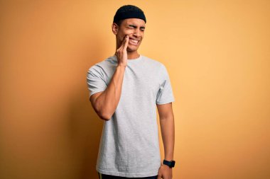 Yakışıklı Afro-Amerikan sporcu sarı arka plan üzerine spor giysisi giyerek diş ağrısı ya da diş ağrısı yüzünden ağıza acı dolu bir ifadeyle dokunuyor. Dişçi